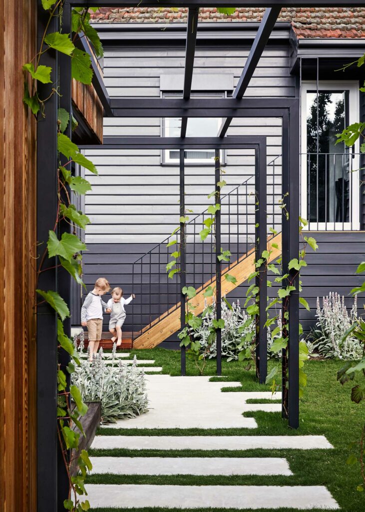 Maike-Design_Next-door-house-2-2 Maike Design backyard. Charcoal painted weatherboard and cedar cladding. Black painted pergola and grape vines. Concrete pavers in lawn