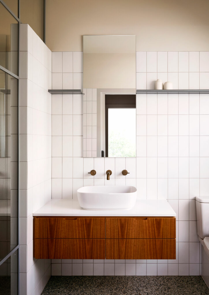 Maike Design bathroom. White tiles, timber joinery and brass tapware. Peach painted ceiling. Terazzo tiles